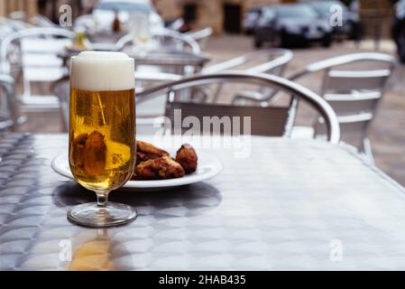 Eiskalte Biere, die auf dem Tisch oder der Terrasse in Gläser gegossen werden, mit einer Tapa aus Hähnchenflügeln. Platz für Kopie Stockfoto