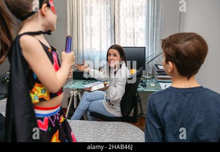 Wütende Mutter schimpft ihre Kinder, die sie bei der Arbeit zu Hause stören Stockfoto