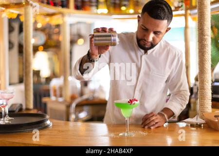 Ein junger mann aus lateinamerika bereitet in einer modernen Cocktailbar sorgfältig ein alkoholisches Getränk zu. Platz für Text. Selektiver Fokus. Stockfoto