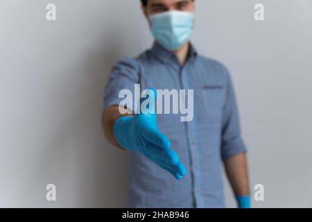 Mann mit Gesichtsschutzhandschuhen streckt den Arm zum Händeschütteln aus Stockfoto