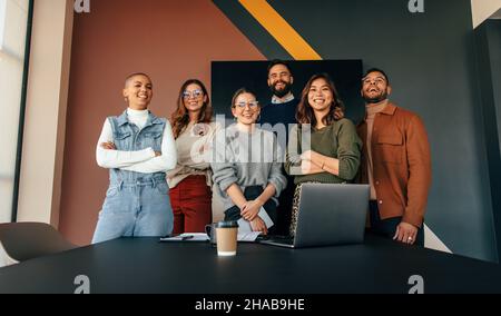 Ein Team aus verschiedenen Geschäftsleuten, die lächeln an der Kamera, während sie hinter einem Tisch in einem Sitzungssaal stehen. Gruppe erfolgreicher Unternehmer, die zusammenarbeiten Stockfoto