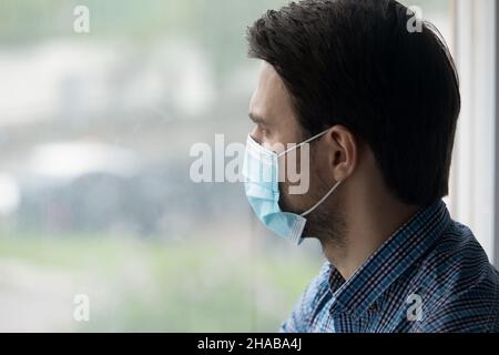 Mann tragen blauen Schutz Gesichtsmaske schaut aus dem Fenster Stockfoto