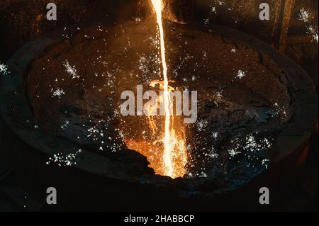 Geschmolzenes Eisen. Flüssiges Metall wird in einem dünnen Strahl in die Schöpfkelle gegossen. Stockfoto