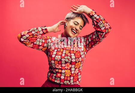 Sorglose junge Frau, die zu ihrem Lieblingslied tanzt. Fröhliche junge Frau, die fröhlich lächelt, während sie schnurlose Ohrhörer trägt. Junge Frau mit gefärbten Haaren Stockfoto