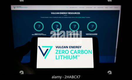 Person, die das Mobiltelefon mit dem Logo des australischen Unternehmens Vulcan Energy Resources Ltd auf dem Bildschirm vor der Webseite hält. Konzentrieren Sie sich auf die Telefonanzeige. Stockfoto
