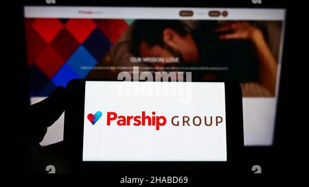 Person, die Smartphone mit Logo der Online-Dating-Firma ParshipMeet Holding GmbH auf dem Bildschirm vor der Website hält. Konzentrieren Sie sich auf die Telefonanzeige. Stockfoto
