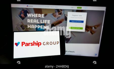 Person, die Mobiltelefon mit Logo der deutschen Online-Dating-Firma ParshipMeet Holding GmbH auf dem Bildschirm vor der Webseite hält. Konzentrieren Sie sich auf die Telefonanzeige. Stockfoto