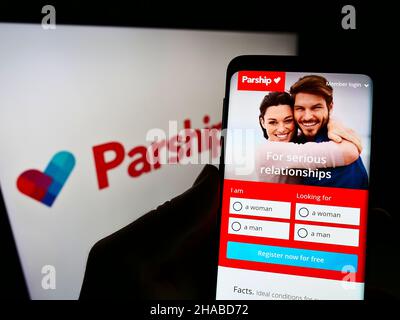 Person, die Mobiltelefon mit der Webseite der Online-Dating-Firma ParshipMeet Holding GmbH auf dem Bildschirm mit Logo hält. Konzentrieren Sie sich auf die Mitte des Telefondisplays. Stockfoto