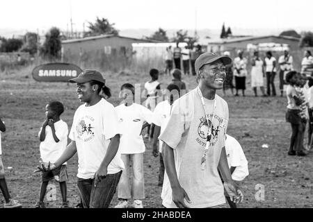 JOHANNESBURG, SÜDAFRIKA - 12. Aug 2021: Eine Graustufenaufnahme des Volunteer Soccer-Trainers, der mit jungen afrikanischen Kindern auf dem Schulhof arbeitet. Stockfoto