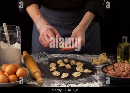 Ein Mann modelliert ein traditionelles russisches Gericht, Knödel, Milch in einem Krug und Mehl, Hühnereier und einen Teller mit Hackfleisch, Mehl in einem Krug und Olivenöl Stockfoto