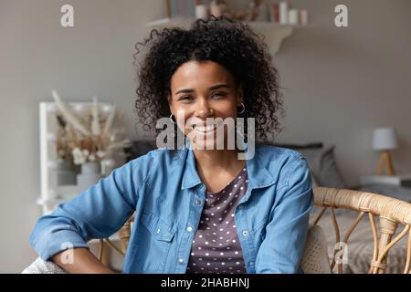 Attraktive afrikanische Frau sitzt auf dem Sessel und schaut auf die Kamera Stockfoto