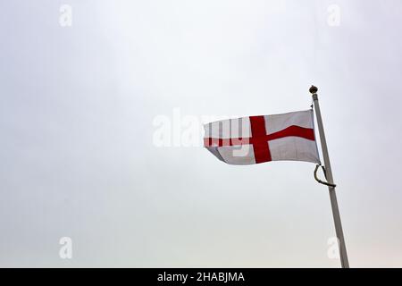 Die Kreuzfahne von St. George ist vor einem reinen weißen Himmel isoliert Stockfoto