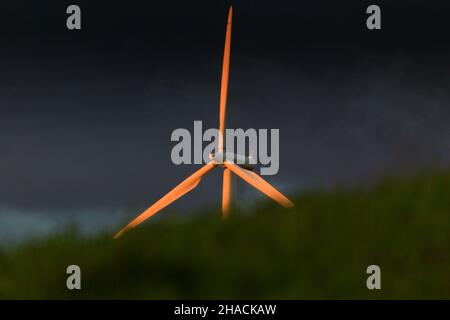 Windturbine, beleuchtet von untergehenden Sonnenstrahlen, mit stürmischem Himmel im Hintergrund, Niedersachsen, Deutschland Stockfoto