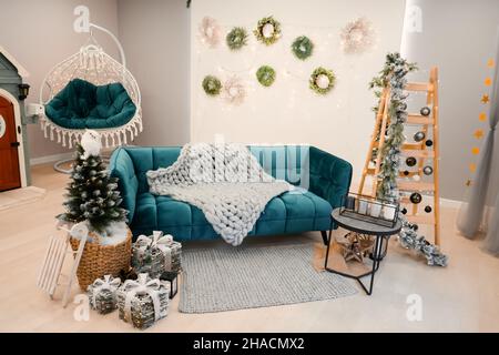 Stilvolles weihnachtliches Wohnzimmer mit grünem Sofa, weihnachtsbaum und -Kranz, Sternen, Geschenken und Dekoration. Stockfoto