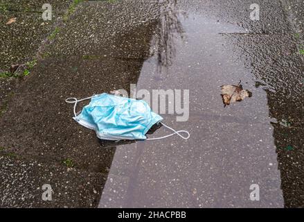 Gesichtsmaske zum Schutz vor dem kovidierten Virus wurde weggeworfen und liegt in einer Pfütze auf der Straße Stockfoto