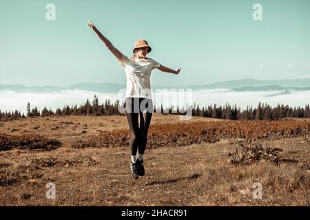 Weibliche Touristen springen in die Natur. Erstaunliche Karpaten Landschaft Hintergrund Banner mit Hügeln, Wolken und Wald in der Dämmerung im Herbst Stockfoto