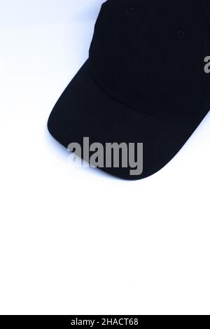 Schräge Aufnahme Einer schwarzen Mütze in der Ecke eines minimalistisch-weißen Hintergrunds, Portrait-Modus Stockfoto