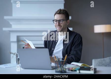Junger, verfeinerter männlicher Unternehmer mit Brille spricht während einer Webkonferenz über das Internet Stockfoto
