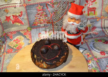 Weihnachtsmann rotes Spielzeug mit Weihnachtsschokolade bedeckt Apfelkuchen im Vordergrund auf Holz-Mittelstück und Happy New Year Tischdecke im Hintergrund. Stockfoto