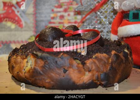 Weihnachts-Schokoladen-Apfelkuchen mit rotem herzförmigem Band darauf und dem roten Weihnachtsmann-Kleid dahinter Stockfoto