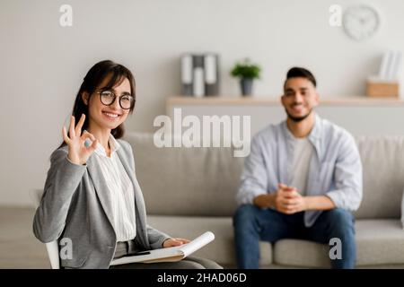 Erfolgreiche Therapie. Professionelle junge Psychologin gestiking okay Zeichen arbeiten mit tausendjährigen arabischen Mann Stockfoto