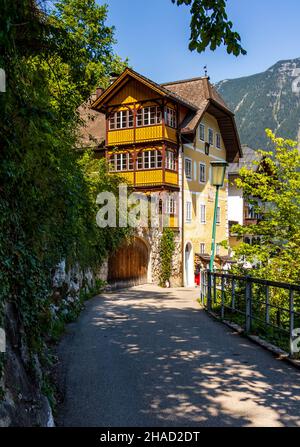 Straße, die an einem sonnigen Sommertag den Weg zu einem schönen, hellen, gelben Gebäude in Hallstatt, Österreich, führt Stockfoto