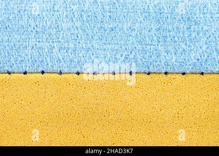 Hintergrund aus einem Makrofoto eines blauen und gelben Schwamms zum Waschen von Glas und Geschirr, die Naht ist sichtbar. Stockfoto