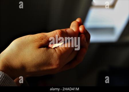 Frau schröpfte Hände im Licht auf einem dunklen Hintergrund, bereit, etwas in ihre Handflächen zu bekommen. Religiöses Konzept, Eucharistie empfangen Stockfoto