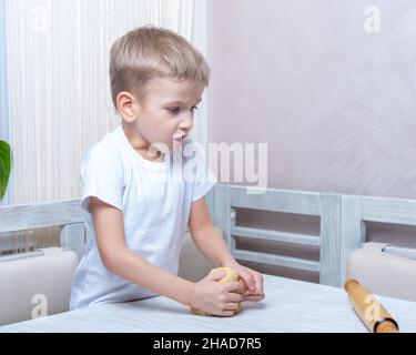 Kochen von traditionellen Lebkuchen. Emotionaler Junge knetet rohen Teig, um Kekse zu machen. Kind hilft Mama beim Weihnachtskochen Stockfoto