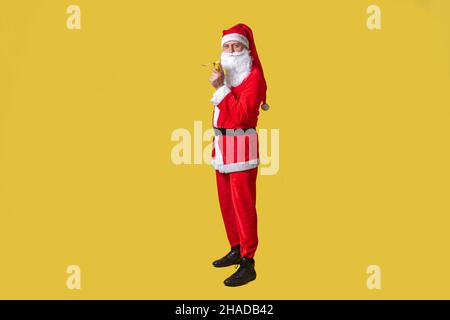 weihnachtsmann gelb lustig groß, Person Spaß glücklich. Der modische bärtige Kaukasier frisst mit der rechten Hand eine Banane Stockfoto
