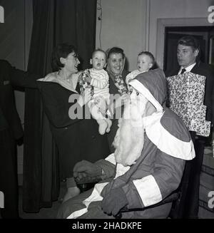 1965, historisch, zwei Mütter mit Kleinkindern lächeln, als der weihnachtsmann mit einem falschen Bart und einer Maske auf seinem Schlitten enthüllt wird, Fife, Schottland, Großbritannien. Stockfoto