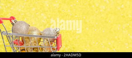 Warenkorb mit goldenen Kugeln auf gelbem Hintergrund mit Kopierfläche, Bannerkonzept für Weihnachten und Neujahr Shopping und Verkauf. Stockfoto
