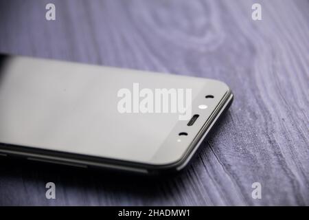 Ein schwarzes modernes Smartphone mit Kamera. Nahaufnahme auf blauem Holztisch Stockfoto