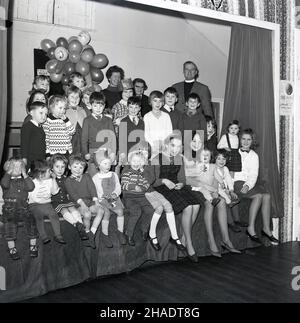 1965, historisch, Gruppe von Kindern, unterschiedlichen Alters, sitzen zusammen auf der Bühne in Longwick Village Hall, Buckiinghamshire, Großbritannien nach der Weihnachtsfeier Stockfoto