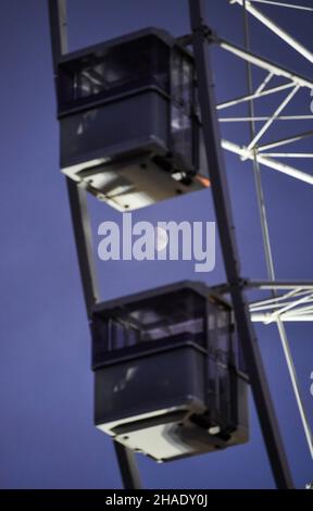 Brighton UK 12th December 2021 - hinter dem großen Beobachtungsrad im Zentrum des Brighton Christmas Festival und fayre guckt der Mond durch Wolken : Credit Simon Dack / Alamy Live News Stockfoto