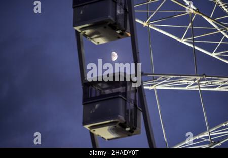 Brighton UK 12th December 2021 - hinter dem großen Beobachtungsrad im Zentrum des Brighton Christmas Festival und fayre guckt der Mond durch Wolken : Credit Simon Dack / Alamy Live News Stockfoto