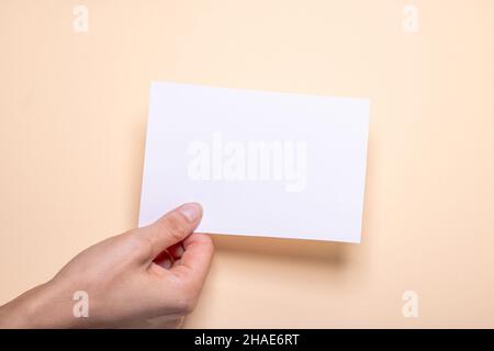 Die weibliche Hand hält ein leeres Stück Papier mit Kopierraum vor einem cremefarbenen Hintergrundkarton Stockfoto