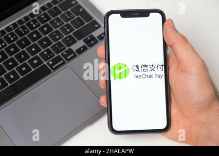 WeChat Pay Finanzplattform für Geldtransfers mit dem Smartphone. Man Hand hält ein Mobiltelefon mit Anwendung auf dem Bildschirm und Notebook auf dem Hintergrund. November 2021, San Francisco, USA Stockfoto