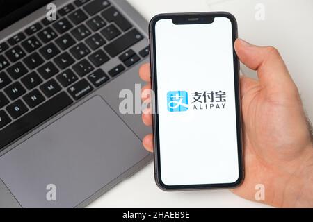 Alipay Finanzplattform für Geldtransfers mit dem Smartphone. Man Hand hält ein Mobiltelefon mit Anwendung auf dem Bildschirm und Notebook auf dem Hintergrund. November 2021, San Francisco, USA Stockfoto