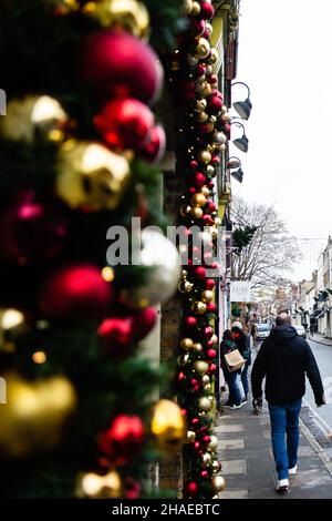 Eton, Großbritannien. 12th. Dezember 2021. In der Eton High Street passieren Menschen lokale Geschäfte, die zu Weihnachten geschmückt sind. Laut dem Office of National Statistics (ONS) geben britische Haushalte mehr für Waren und weniger für Dienstleistungen aus, während sich die Omicron-Coronavirus-Variante ausbreitet. Kredit: Mark Kerrison/Alamy Live Nachrichten Stockfoto