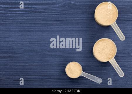 Schaufeln gefüllt mit Proteinpulver auf blauem Hintergrund Holz Stockfoto