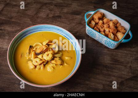 Fischsuppe, basierend auf Garnelen, Muscheln, Muscheln, Seehecht und Tintenfisch, Begleitet von gebratenem Brot auf einem dunklen Holztisch. Stockfoto