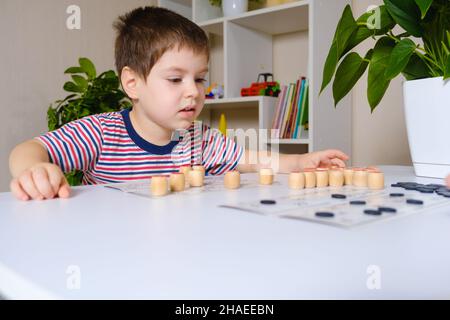 Ein 4-jähriger Junge spielt loto und studiert Zahlen anhand eines Brettspiels. Für Text platzieren. Stockfoto