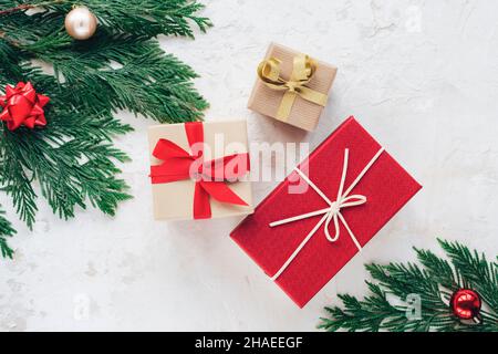 Weihnachtsgeschenkschachteln, verziert mit Bändern. Tannenzweige mit roten und goldenen Kugeln auf weißem strukturiertem Hintergrund. Draufsicht, flach liegend. Stockfoto