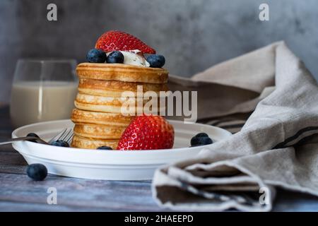 Klare Sicht auf Stapel von Pfannkuchen mit Honigstock, Erdbeere, Blaubeere und Peitschencreme auf dem Teller, leckeres Dessert mit Milch zum Frühstück. Stockfoto