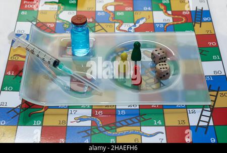 Medizinische Spritze und Impffläschchen auf Schlangen und Leitern Brettspiel mit Würfeln. Konzept der Anzahl der benötigten Impfdosen und Booster. Irland Stockfoto