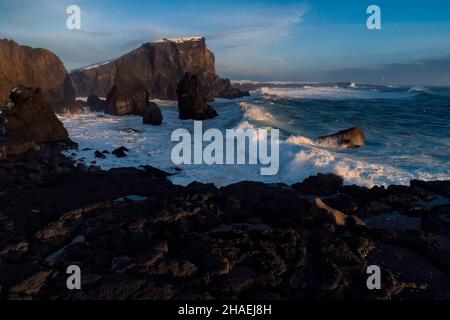 Massive Wellen schlagen nach einem Wintersturm im Nordatlantik gegen große Felsformationen in Island, Sonnenuntergang aproaching backlighting the bre Stockfoto