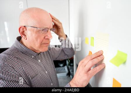 Ältere Mann an Noten suchen. Forgetful Senior mit Demenz, Memory Problem, Gesundheit Konzept Stockfoto