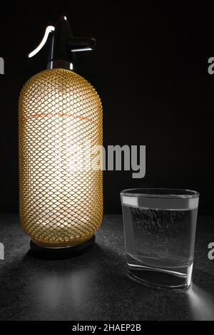 Vertikale, breite Studioaufnahme mit beleuchtetem, luxuriös aussehendem Vintage-Sodasiphon mit goldenem Gehäuse auf einem Schreibtisch aus Stein. Glas Soda. Stockfoto