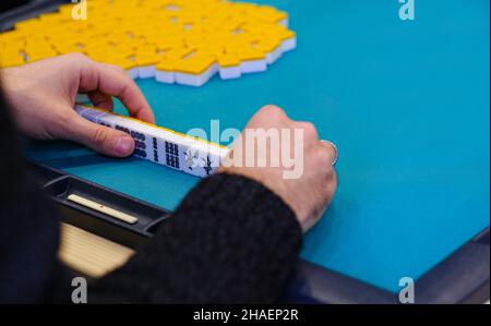 Ein Mahjong-Tisch mit einem aktiven Spiel und den Händen eines Spielteilnehmers. Speicherplatz kopieren. Ein altes asiatisches Spiel namens Mahjong als eine Möglichkeit, sich zu entspannen und Stockfoto